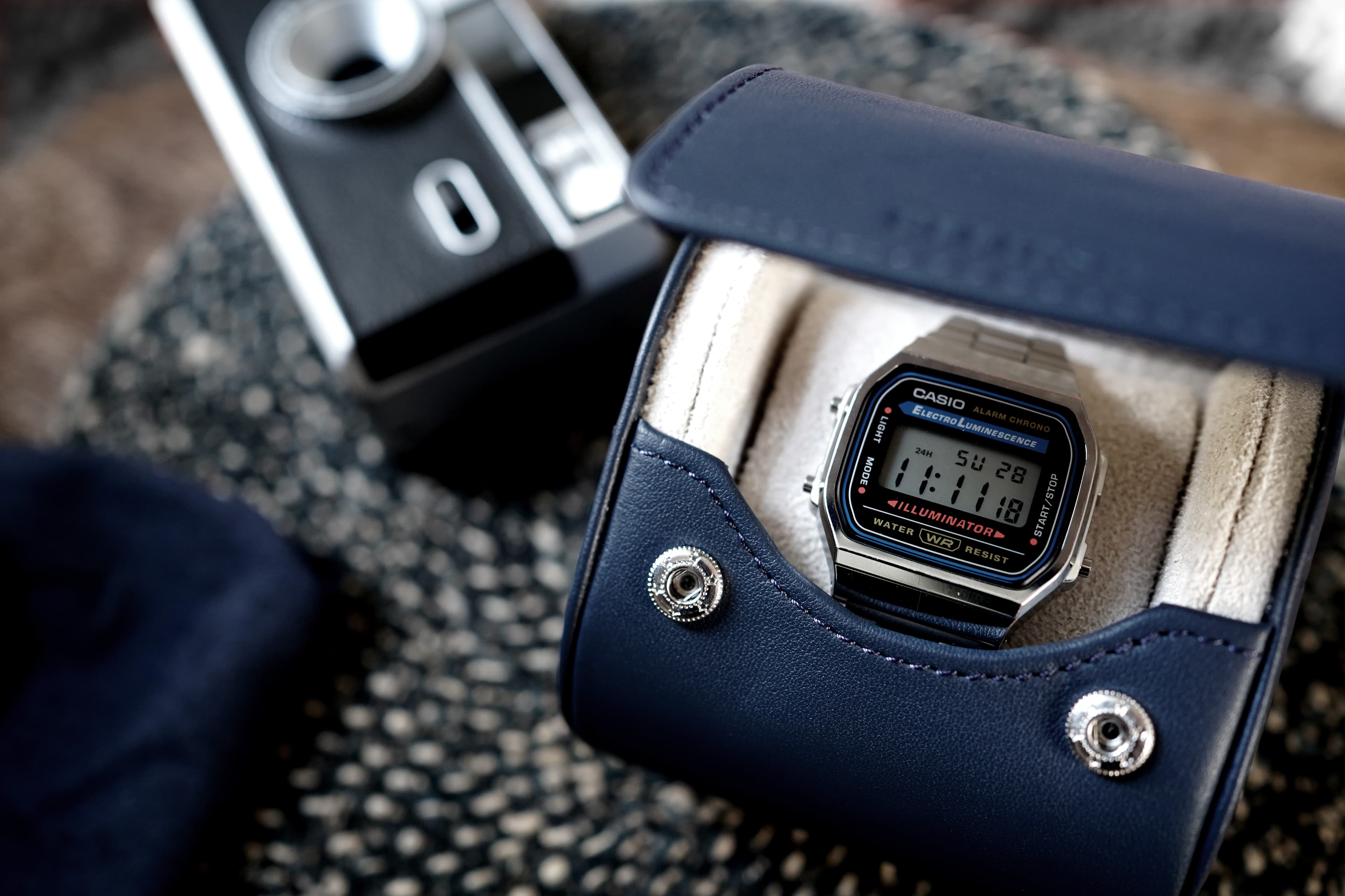 Discover the fusion of urban charm and luxury with our Midnight Navy Blue Watch Travel Roll. This meticulously crafted accessory, adorned with a sumptuous Cream Microfiber Interior, ensures your watches travel in style. In this striking scene, our watch roll takes center stage against a vibrant graffiti-covered wall. The juxtaposition of gritty street art and refined craftsmanship creates a unique and captivating image. Whether you're an avid traveler or a watch aficionado, this premium accessory embodies both function and fashion, offering a secure and stylish haven for your timepieces.