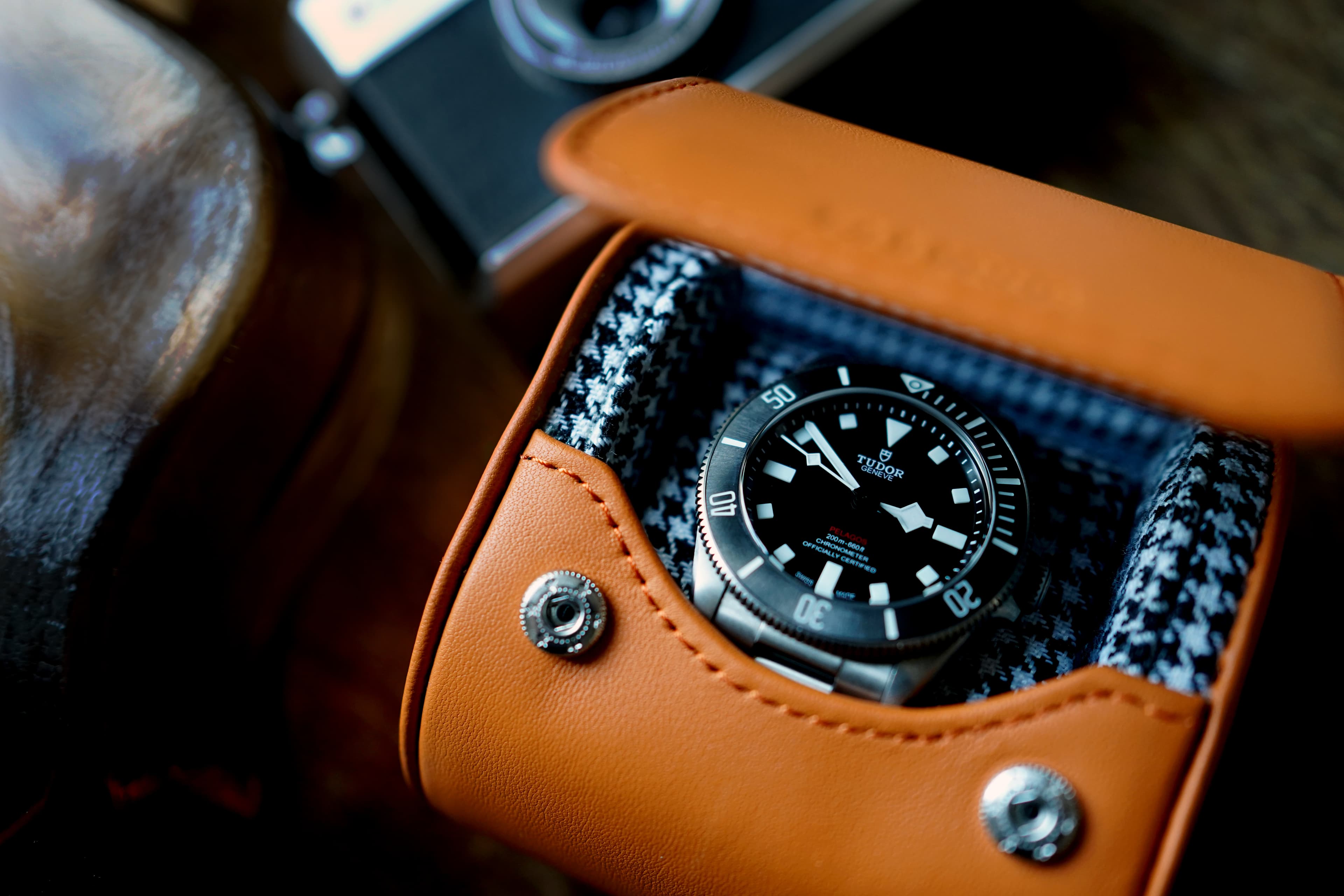 Elevate your watch collection to new heights with our Icon case, a masterpiece of luxury and style. The Icon case features a vibrant Orange Leather exterior and a sophisticated Houndstooth Cotton interior, creating an exquisite blend of fashion and function. In this captivating image, our Icon case graces an outdoor table alongside a stainless steel wine chiller, all set against the backdrop of a charming glamping site. An inviting garden chair completes the scene, beckoning you to experience the epitome of refinement in the great outdoors. Discover the perfect home for your cherished timepieces with this iconic watch case, where elegance meets innovation.